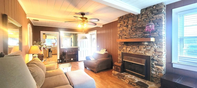 living room with ceiling fan, hardwood / wood-style floors, beam ceiling, wooden walls, and a stone fireplace