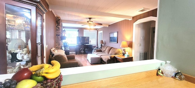 living room with beam ceiling, wooden ceiling, ceiling fan, and wood walls