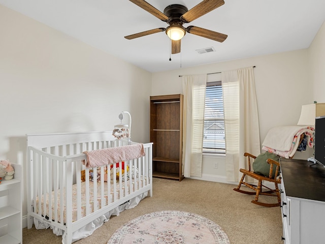 bedroom featuring light carpet, a nursery area, and ceiling fan