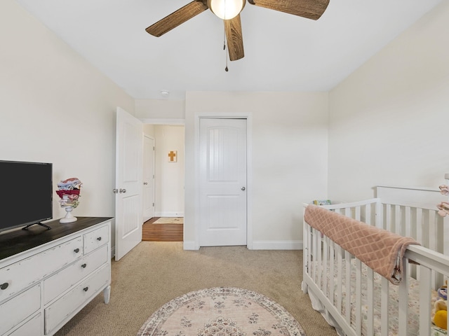 carpeted bedroom featuring a nursery area and ceiling fan