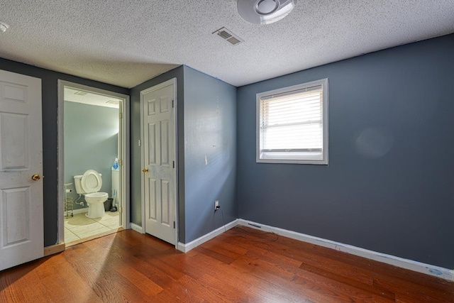 unfurnished bedroom featuring hardwood / wood-style flooring, connected bathroom, and a textured ceiling