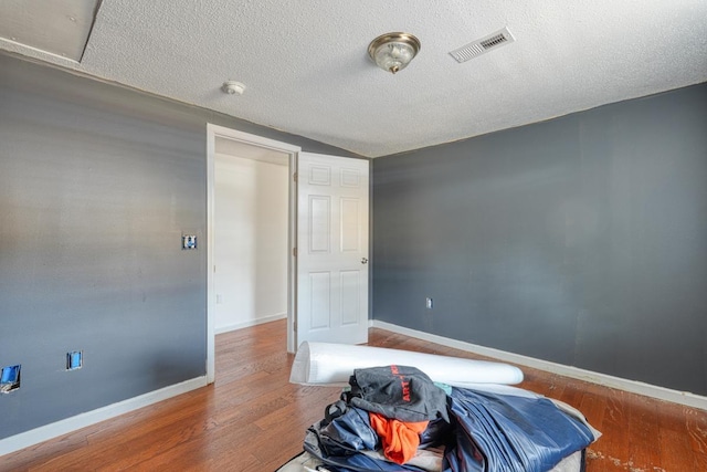 bedroom featuring vaulted ceiling, hardwood / wood-style floors, and a textured ceiling