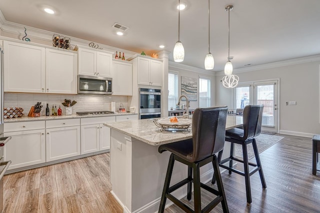 kitchen with a breakfast bar, appliances with stainless steel finishes, white cabinets, a center island with sink, and decorative light fixtures