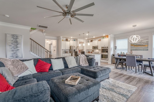 living room with crown molding, ceiling fan with notable chandelier, and light hardwood / wood-style flooring