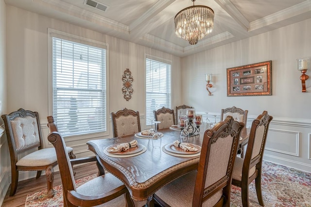 dining area with wood-type flooring, ornamental molding, coffered ceiling, a notable chandelier, and beam ceiling