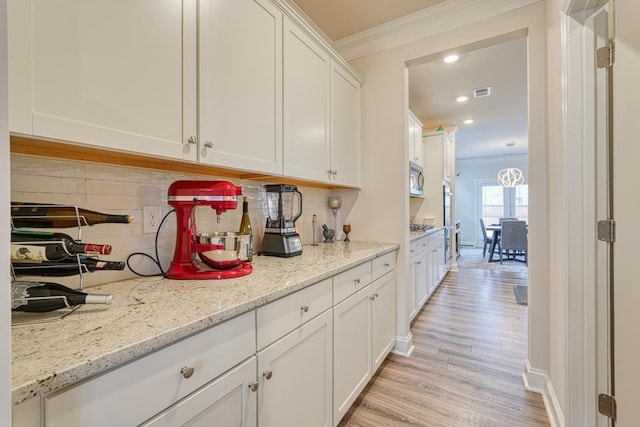 kitchen with tasteful backsplash, white cabinetry, ornamental molding, light stone counters, and light hardwood / wood-style flooring