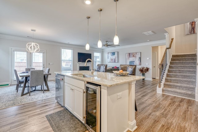 kitchen featuring sink, white cabinetry, hanging light fixtures, a center island with sink, and beverage cooler