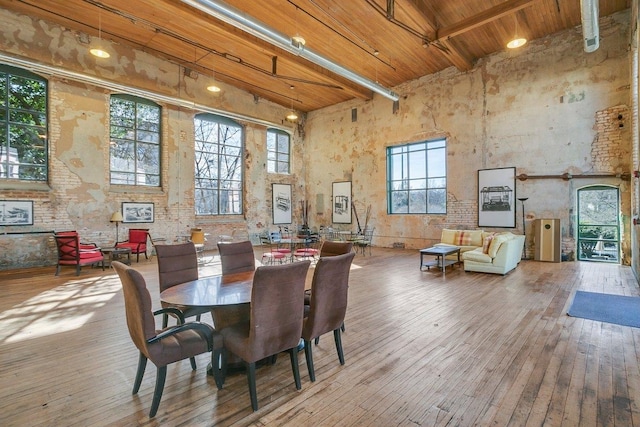 dining space featuring beamed ceiling, a towering ceiling, hardwood / wood-style floors, and wooden ceiling