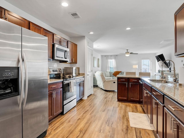 kitchen with appliances with stainless steel finishes, decorative backsplash, ceiling fan, light hardwood / wood-style floors, and light stone countertops