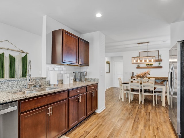 kitchen with sink, pendant lighting, stainless steel appliances, light stone countertops, and decorative backsplash