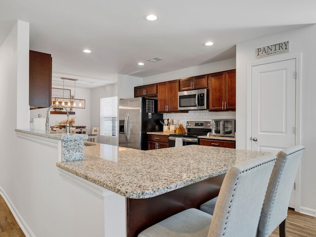 kitchen with appliances with stainless steel finishes, a breakfast bar area, hanging light fixtures, kitchen peninsula, and light stone countertops