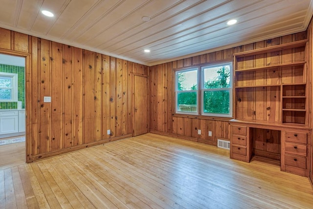 spare room with crown molding, wooden walls, a wealth of natural light, and light wood-type flooring