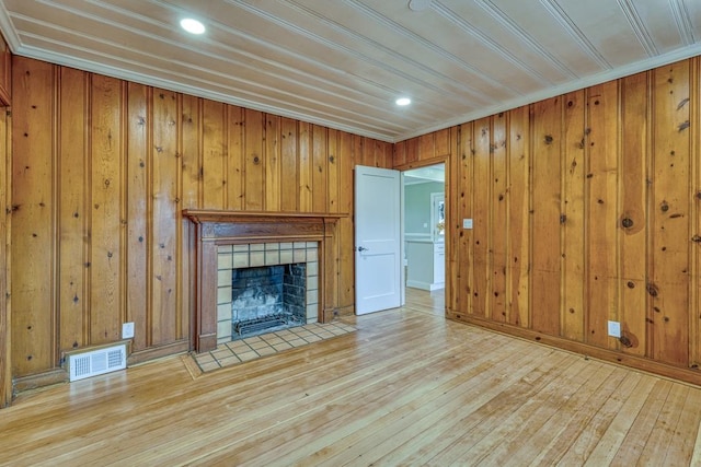 unfurnished living room with a tiled fireplace, crown molding, wooden walls, and light hardwood / wood-style floors