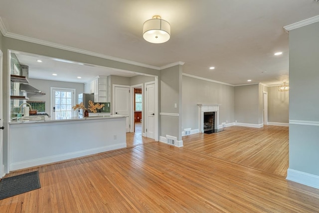 unfurnished living room with sink, light hardwood / wood-style flooring, and ornamental molding