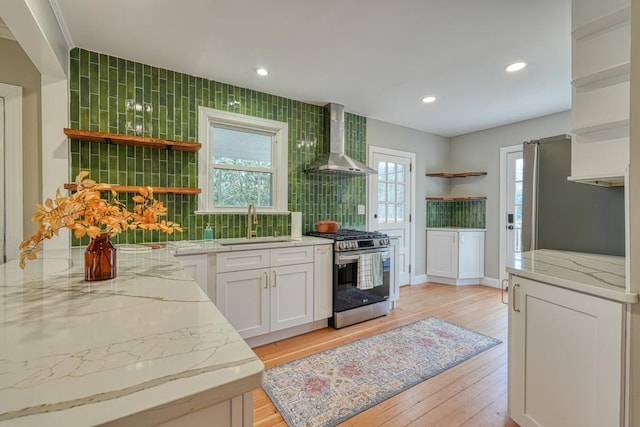 kitchen with white cabinetry, sink, light stone counters, stainless steel appliances, and wall chimney exhaust hood