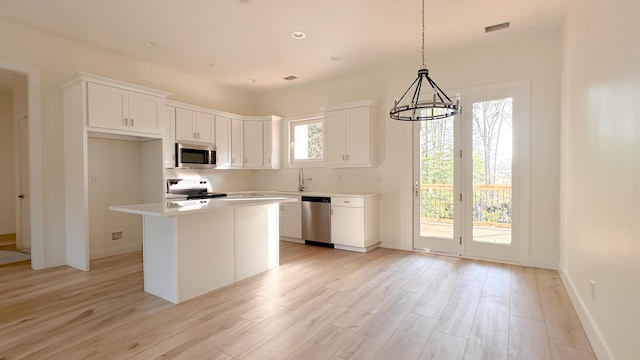 kitchen with appliances with stainless steel finishes, white cabinetry, hanging light fixtures, a center island, and light wood-type flooring