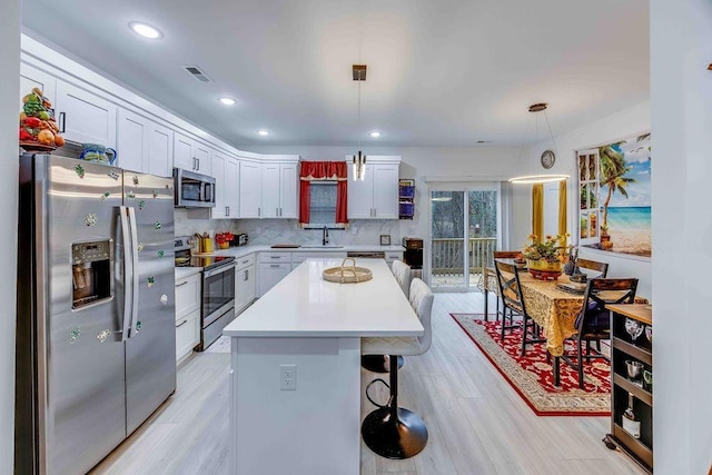 kitchen with pendant lighting, appliances with stainless steel finishes, a kitchen island, and white cabinets