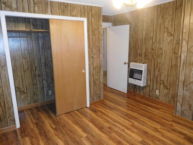 unfurnished bedroom featuring dark wood-type flooring, heating unit, wood walls, and a closet