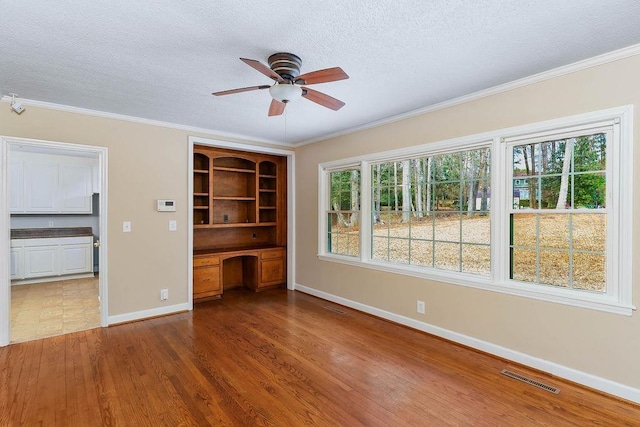 interior space with hardwood / wood-style floors, crown molding, built in desk, and ceiling fan