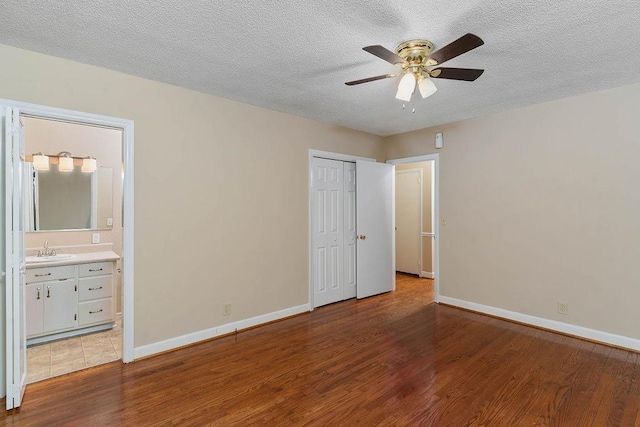 unfurnished bedroom with sink, ensuite bath, wood-type flooring, and ceiling fan