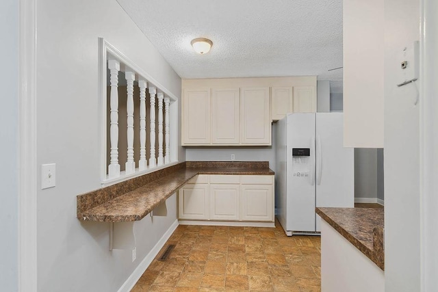 kitchen featuring white refrigerator with ice dispenser, white cabinets, and a textured ceiling