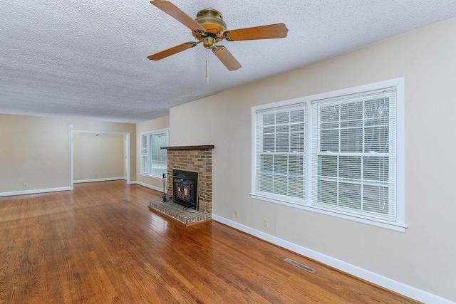 unfurnished living room with hardwood / wood-style flooring, ceiling fan, a fireplace, and a textured ceiling