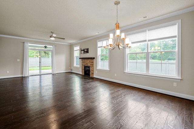 unfurnished living room with dark wood-type flooring, ornamental molding, a stone fireplace, and ceiling fan with notable chandelier