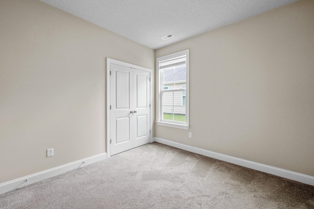 empty room with light colored carpet and a textured ceiling