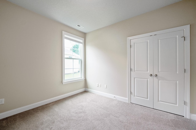 unfurnished bedroom with light colored carpet, a closet, and a textured ceiling