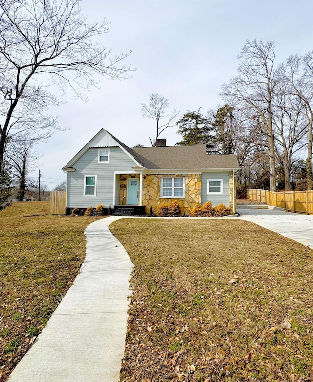 view of front of house featuring stone siding, a chimney, fence, and a front yard