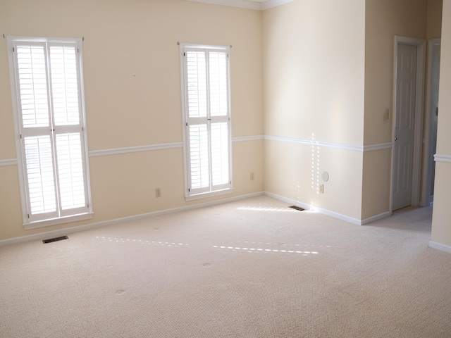 spare room with a wealth of natural light, ornamental molding, and light colored carpet