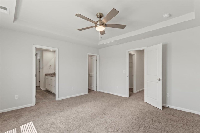 unfurnished bedroom featuring ceiling fan, ensuite bath, a raised ceiling, and light colored carpet