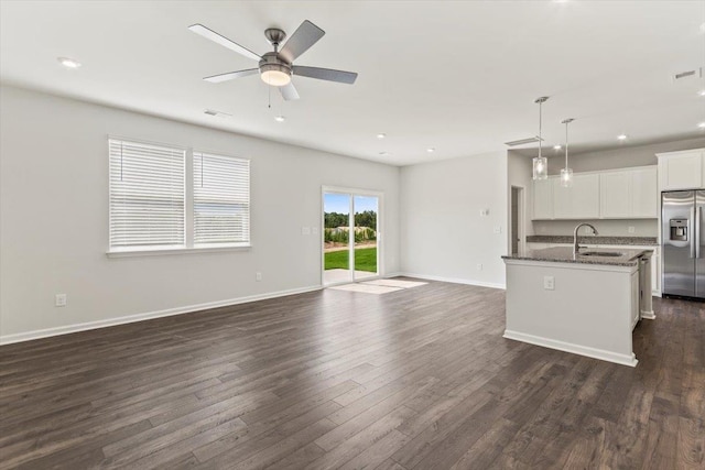 kitchen with sink, stainless steel fridge with ice dispenser, a center island with sink, dark stone countertops, and white cabinets