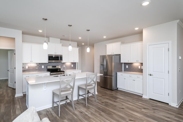 kitchen with dark wood-type flooring, white cabinetry, pendant lighting, stainless steel appliances, and a kitchen island with sink