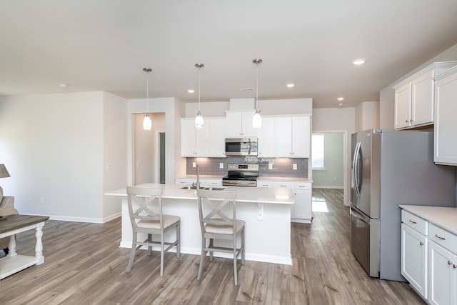 kitchen with appliances with stainless steel finishes, white cabinetry, backsplash, an island with sink, and decorative light fixtures