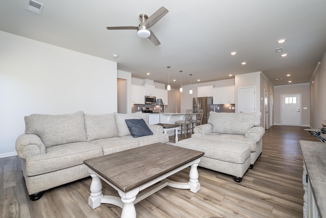 living room featuring ceiling fan, ornamental molding, sink, and light hardwood / wood-style floors