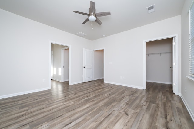 unfurnished bedroom with ceiling fan, a walk in closet, dark hardwood / wood-style floors, and a closet