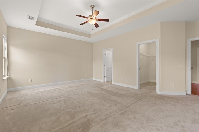 unfurnished bedroom with crown molding, a spacious closet, a raised ceiling, a closet, and ceiling fan