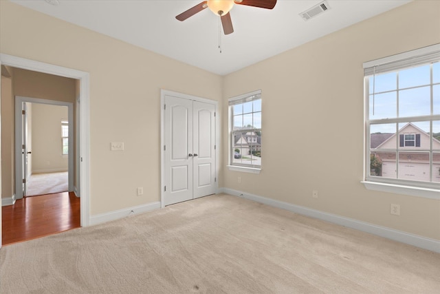 unfurnished bedroom with multiple windows, light colored carpet, a closet, and ceiling fan