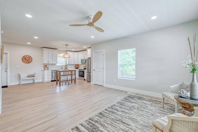 living room with light hardwood / wood-style flooring, sink, a wealth of natural light, and ceiling fan