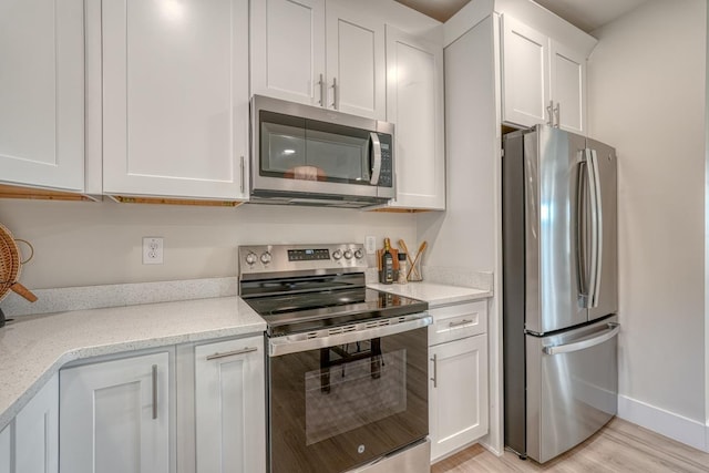 kitchen featuring light stone countertops, stainless steel appliances, white cabinets, and light wood-type flooring