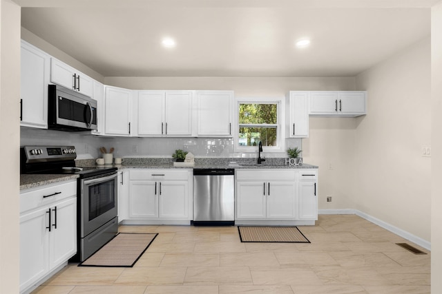 kitchen featuring sink, white cabinets, backsplash, stainless steel appliances, and light stone countertops