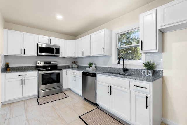 kitchen with appliances with stainless steel finishes, sink, white cabinets, dark stone counters, and decorative backsplash