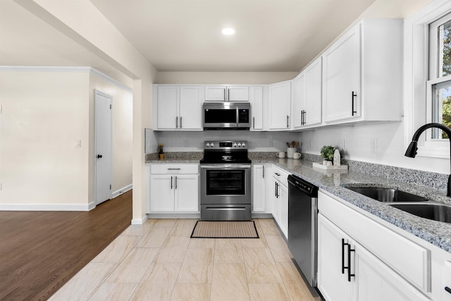 kitchen with sink, light stone counters, white cabinets, stainless steel appliances, and backsplash