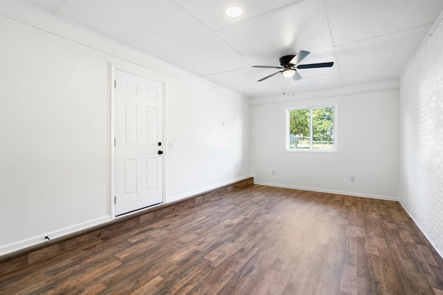 empty room with dark hardwood / wood-style floors, ceiling fan, and brick wall