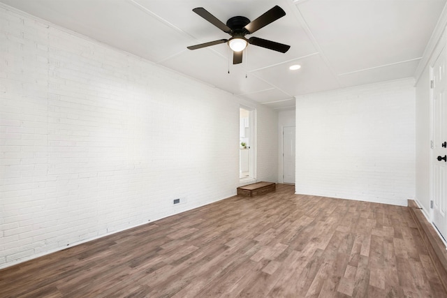 unfurnished room with hardwood / wood-style flooring, ceiling fan, and brick wall