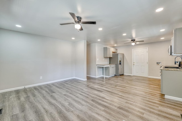 unfurnished living room featuring ceiling fan, sink, and light wood-type flooring