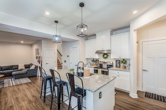 kitchen with stainless steel electric range oven, a kitchen breakfast bar, light stone countertops, a kitchen island with sink, and white cabinets