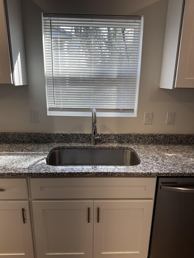 kitchen featuring dark stone countertops, black dishwasher, sink, and white cabinets