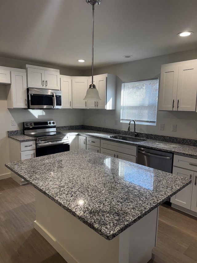 kitchen featuring appliances with stainless steel finishes, decorative light fixtures, sink, white cabinets, and a center island